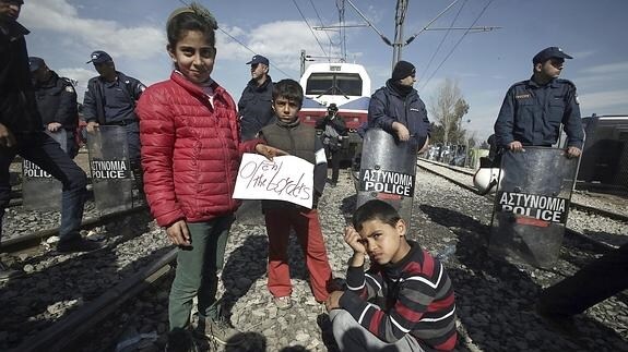 Niños refugiados sirios muestran un cartel en el que piden la apertura de las fronteras.