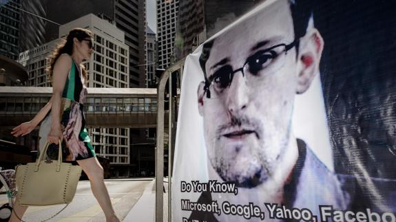 Una mujer camina ante un cartel con la cara de Snowden.