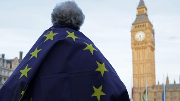 Un hombre con una bandera europea sobre la espalda mira al Big Ben. 