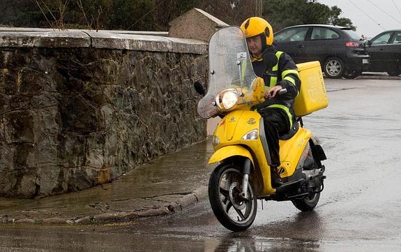 Un cartero lleva a cabo el reparto en una moto de Correos, en Santander.