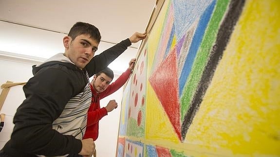 Dos alumnos posan mientras trabajan en un mural.