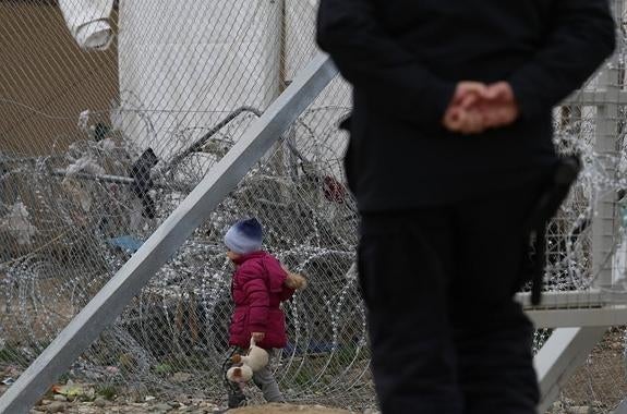 Una niña juega en una alambrada ante la mirada de un vigilante del campo de refugiados. 