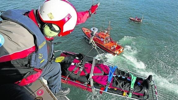 El helicóptero del Gobierno de Cantabria iza la camilla con un muñeco que simula un herido rescatado por la Salvamar junto a las aguas de la isla de Santa Marina.