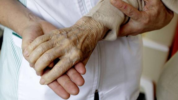 Un cuidador sostiene la mano de un enfermo.