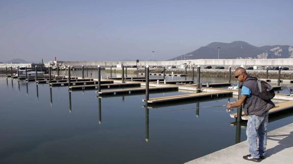 Un hombre pesca junto a los pantalanes vacíos del Puerto de Laredo, cuya concesión ha recuperado el Gobierno.