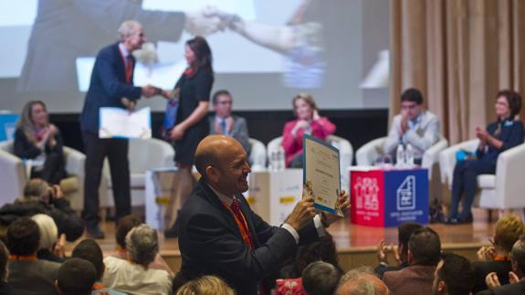 Uno de los galardonados enseña el diploma que acaba de recoger mientras, en el escenario, el presidente de Unicef, Carmelo Angulo, entrega otro.