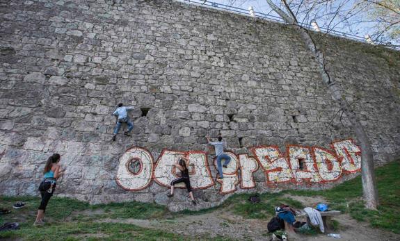 Un grupo de aficionados a la escalada practica sobre la pared de Los Peligros, en la que destaca el enorme grafiti. 