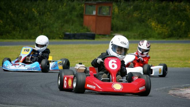 Participantes en una carrera infantil de karts toman una curva a todo gas.