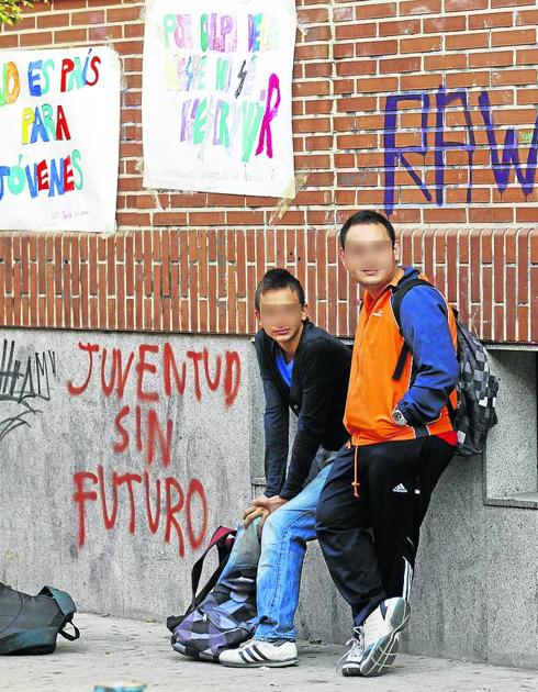 Estudiantes apoyados en un muro lleno de pintadas. 