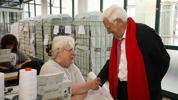 El Padre Ángel, ataviado con su característica bufanda roja, visita las instalaciones del taller de confección de ropa de Amica en Torrelavega. 