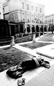 Un pobre duerme en la plaza de Oriente, ante la fachada del Teatro Real, en Madrid.