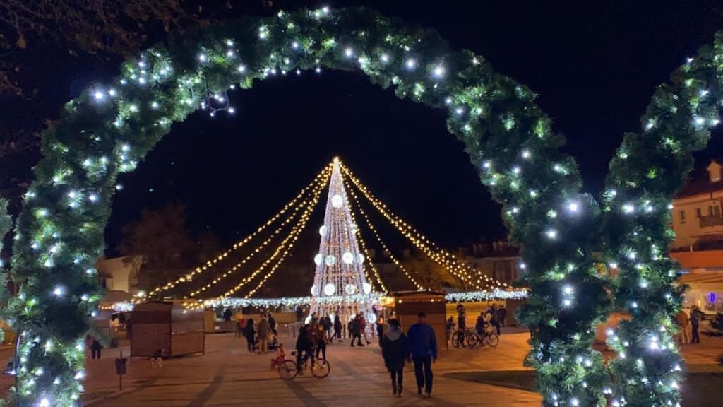 El árbol de Navidad preside el centro de la Plaza España de La Flecha rodeado de los puestos y atracciones que conforman el Mercado de Navidad de Arroyo de la Encomienda. 
