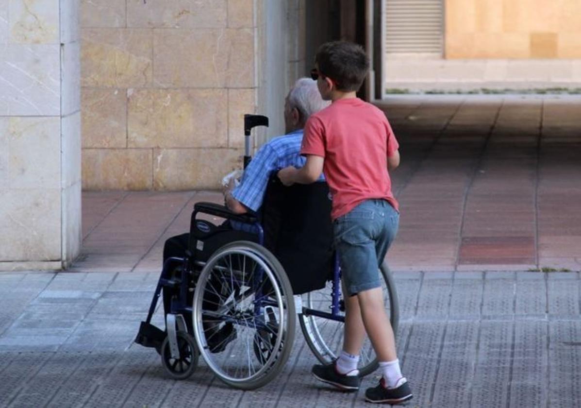 Un niño traslada a un anciano en silla de ruedas.