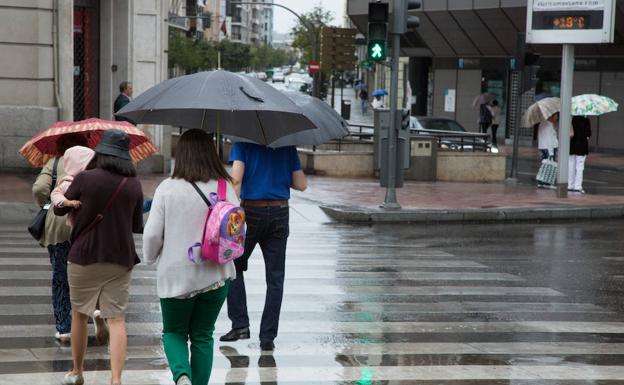 Varias personas caminan bajo la lluvia por Valladolid capital. 