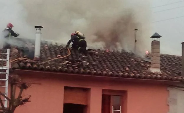 Los bomberos sofocan las llamas desde el tejado de la vivienda.