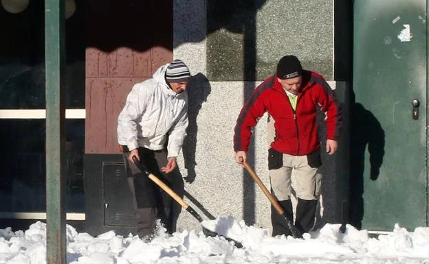 Dos hombres limpian una acera con palas. 
