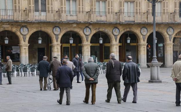 Varias personas mayores charlan distendidamente mientras pasean por la Plaza Mayor