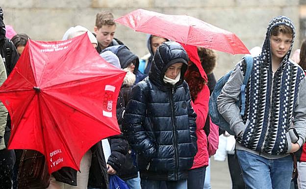 Unos jóvenes pasean por Segovia protegidos con paraguas y chubasqueros ante la incesante lluvia y nieve de este lunes. 