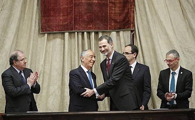 El presidente luso Marcelo Rebelo de Sousa y Felipe VIestrechan sus manos en la mesa presidencial del Paraninfo arropados por los aplausos de Herrera y Rivero. 