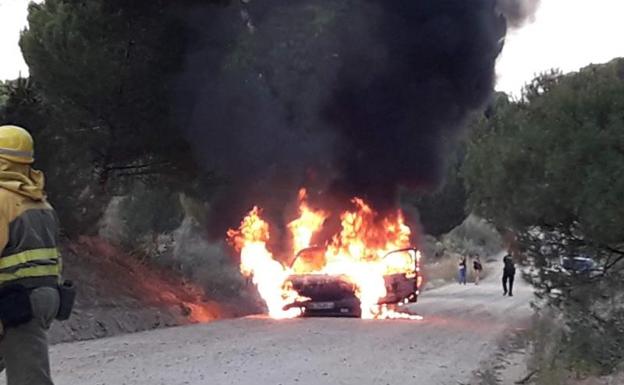 El vehículo incendiado envuelto en llamas y los bomberos durante las labores de extinción.