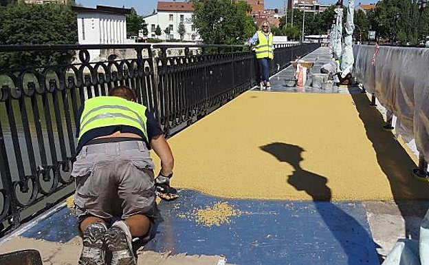 Un trabajador extiende el firme antideslizante en la acera del lateral izquierda del Puente Mayor, en la que ya colocaron días atrás las farolas y la valla protectora. 
