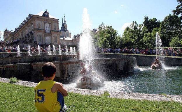 Un niño sentado en el césped observa cómo emergen los chorros de agua en una de las fuentes..