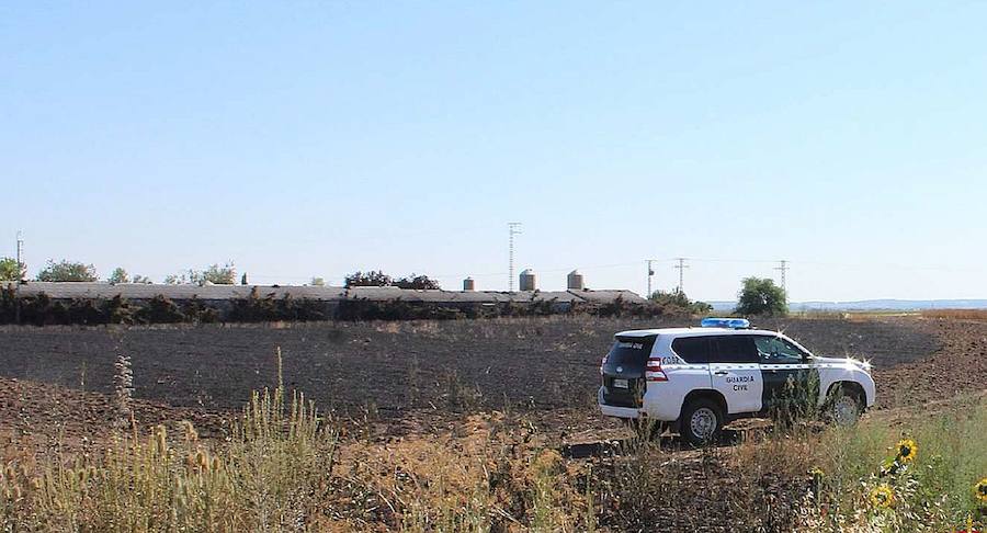 Un coche de la Guardia Civil ante las tierras y la nave afectadas por el fuego.