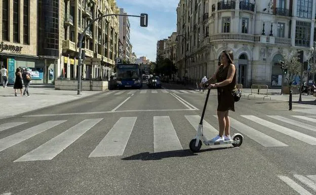 Una mujer cruza la calzada en patinete eléctrico en la Plaza de Zorrilla de Valladolid. 