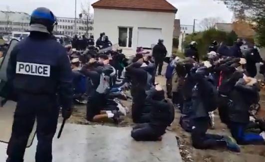 Policías vigilan a los jóvenes, arrodillados en el patio del liceo.