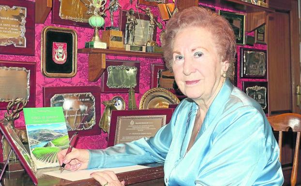 La vallisoletana Eumelia Sanz, ante una pared de su casa en la que conserva 91 trofeos y placas ganadas en certámenes literarios, junto a uno de sus libros publicados, 'Surcos de bonanza. Temas de Castilla y León'.