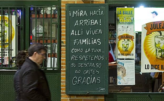 Dos ciudadanos pasean delante del cartel de un bar de Valladolid que pide respeto para el descanso vecinal. 