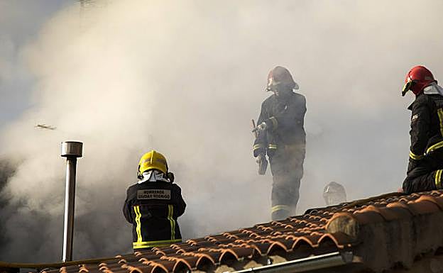 Los bomberos intentan entrar a la vivienda incendiada por el tejado. 