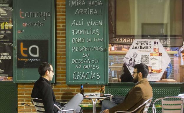 Dos hombres disfrutan en una terraza de un bar de Valladolid que pide respeto para los vecinos con un cartel. 