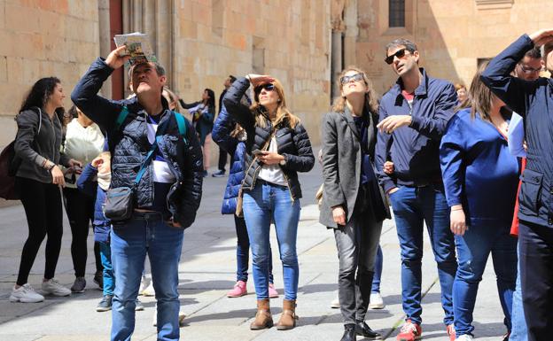 Un grupo de turistas busca la rana de la fachada de la Universidad. 