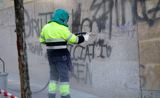 Un operario municipal limpia una pintada en un edificio.