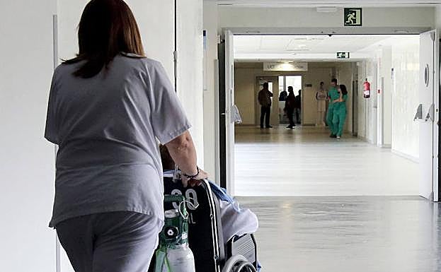 Una sanitaria acompaña a un paciente por un pasillo del Hospital General.