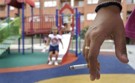 Un adulto fumando en un parque infantil. 