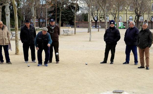 Señores mayores juegan a la petanca en un parque.