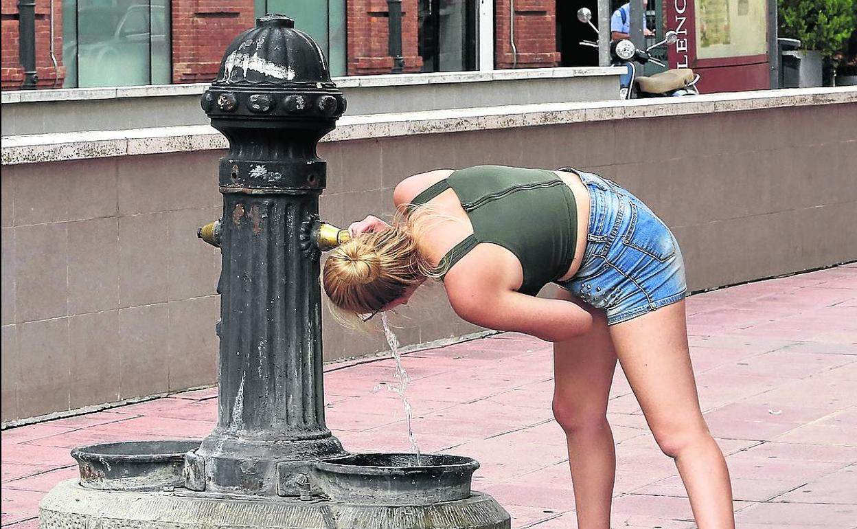 Una joven bebe en una fuente, en el entorno de la plaza de los Juzgados. 