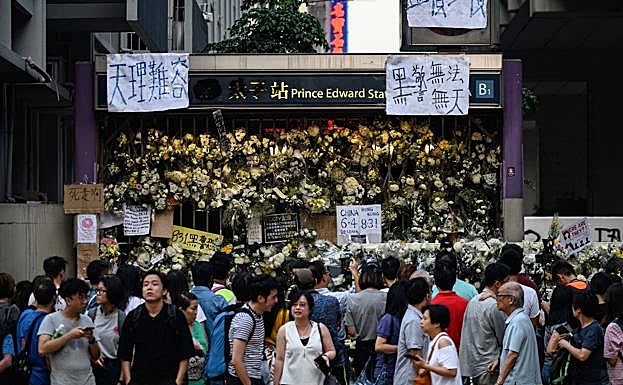 Los peatones esperan para cruzar una calle frente a un monumento improvisado que cubre una entrada de la estación Prince Edward MTR en Hong Kong.