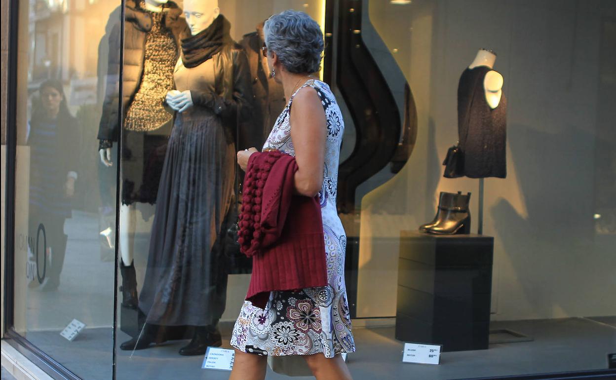 Una mujer pasea en ropa veraniega enfrente de unos escaparates con la temporada de otoño. 