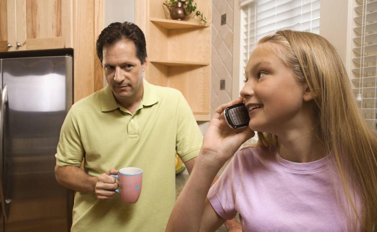 Un padre observa a su hija mientras habla por teléfono. 