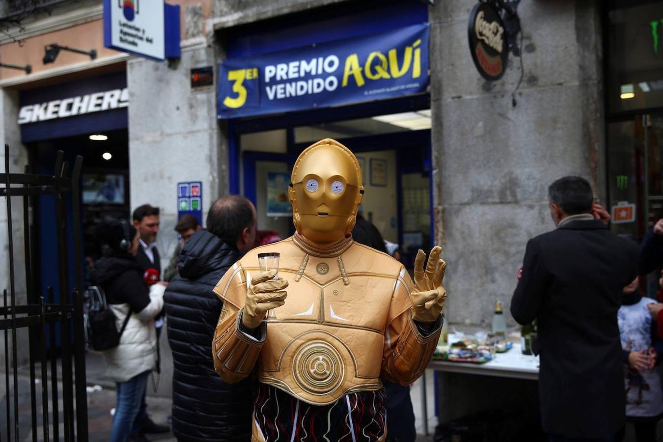 Una persona disfrazada del robot de la Guerra de las Galaxias C-3PO celebra en la administración de lotería 150 en la calle Arenal de Madrid