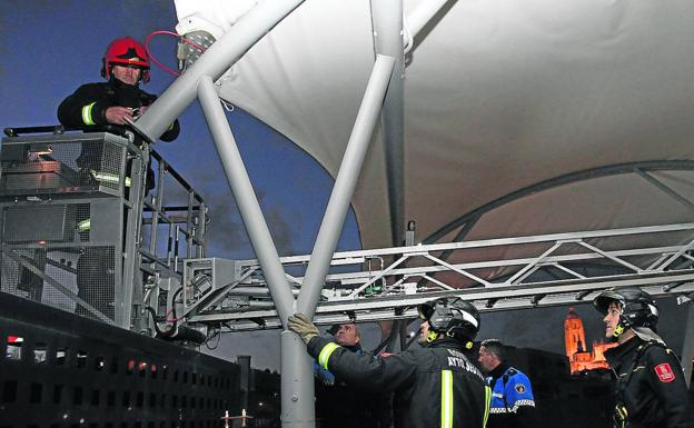 Los bomberos tratan de anclar la lona que cubre la campa de la estación de autobuses. 