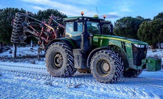 Un tractor parado ante una carretera nevada en las afueras de Ataquines.