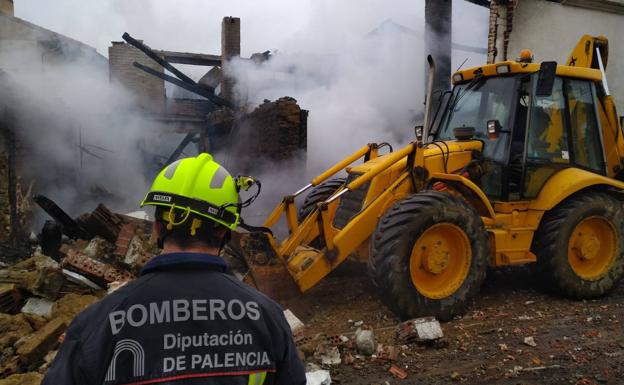 Un bombero refresca la zona mientras una máquina tira la fachada de forma controlada.