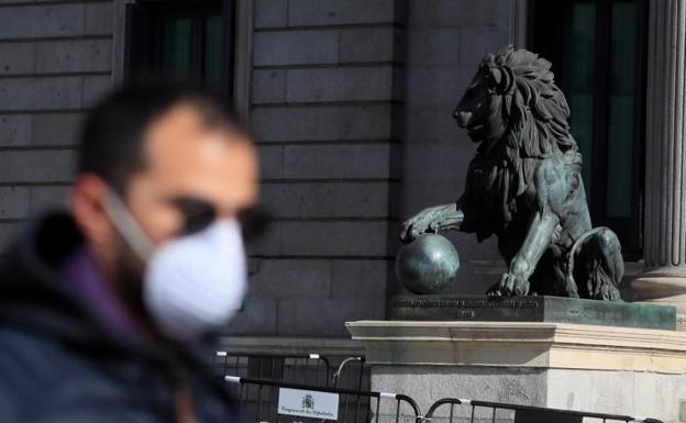 Un hombre con mascarilla pasa frente al Congreso de los Diputados.