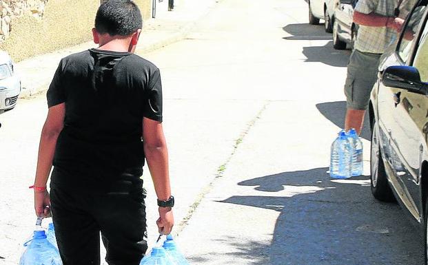 Un niño camina con varias garrafas de agua por una calle de Ochando en agosto de 2019. 