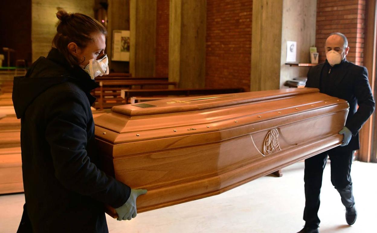 Dos trabajadores de una funeraria conducen un féretro. 