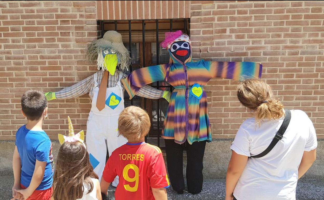 Unos niños contemplan dos de los espantapájaros sujetos a la ventana de una casa de Urueña.